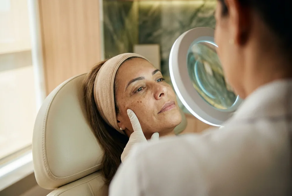 Dermatologista examinando a pele da paciente com lupa antes do biolifting regenerativo